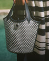A woven black and white handbag is shown in the foreground, with a striped fabric backdrop in the background.