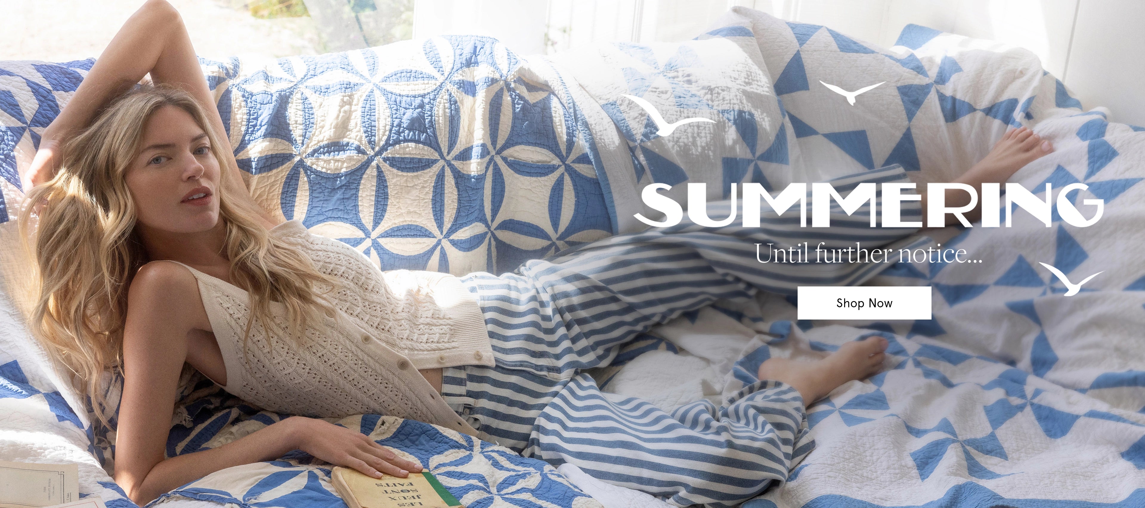 A woman in striped pajamas reclines on a bed covered in blue and white patterned quilts, with the word "SUMMERING" and a "Shop Now" button overlaid on the background.