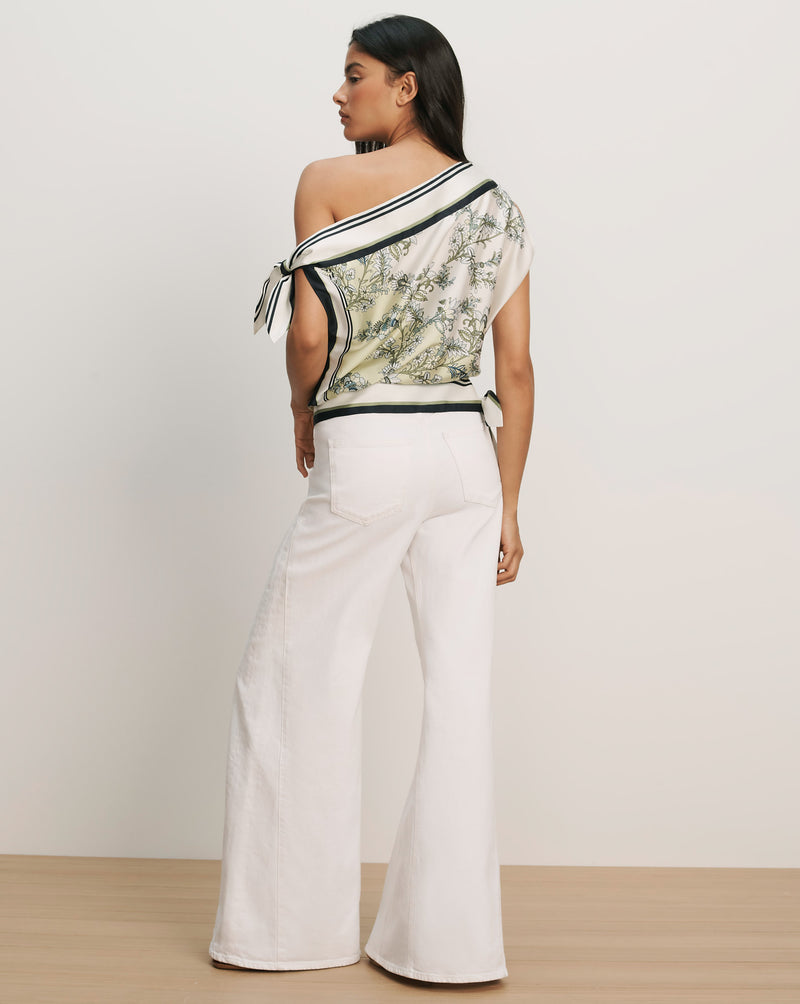 Veronica Beard White off-the-shoulder top with black trim and green floral print, paired with white wide-leg jeans.