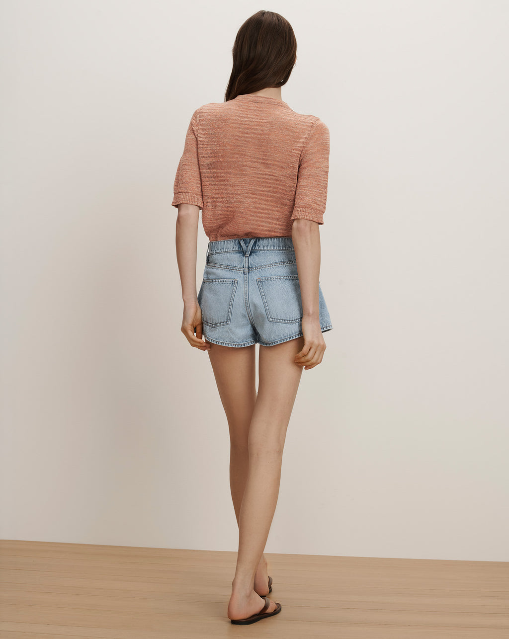 Veronica Beard A woman wears a peach short-sleeve knit top and light wash denim shorts.
