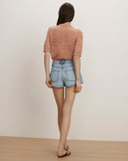 Veronica Beard A woman wears a peach short-sleeve knit top and light wash denim shorts.