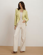 Veronica Beard Light green double-breasted blazer with gold buttons, paired with a cream ribbed tank top and off-white wide-leg jeans.