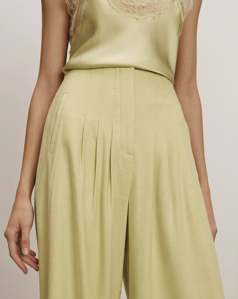 A woman wearing a light yellow sleeveless top and a matching pleated skirt, standing against a plain background.