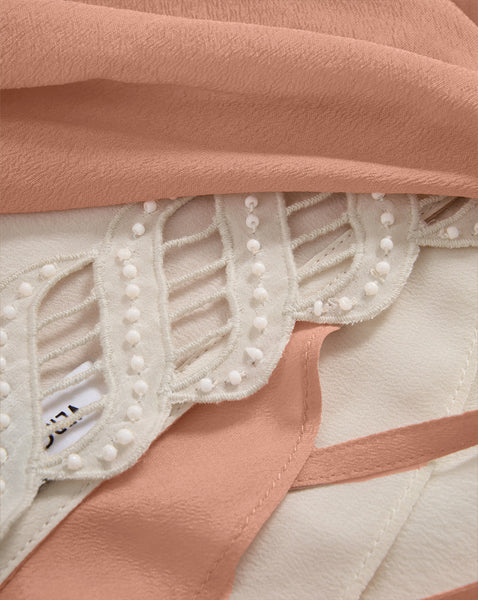 The image shows a close-up view of a delicate, lace-trimmed fabric in a soft, peach color, with a subtle pattern and texture visible.