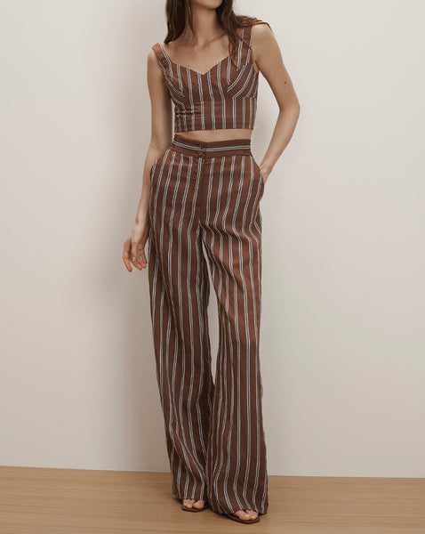 A young woman wearing a striped crop top and matching wide-leg pants stands against a plain, light-colored background.