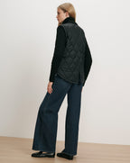 Veronica Beard Black quilted vest over black sweater and wide-leg jeans.