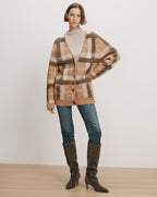 Veronica Beard Tan plaid cardigan, cream turtleneck, blue jeans, brown boots.