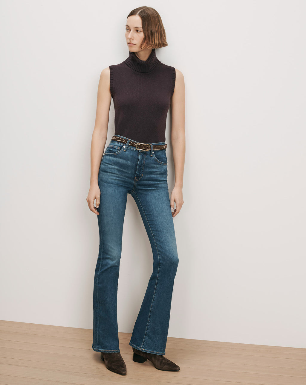 Veronica Beard Dark brown sleeveless turtleneck, blue flare jeans, studded belt.