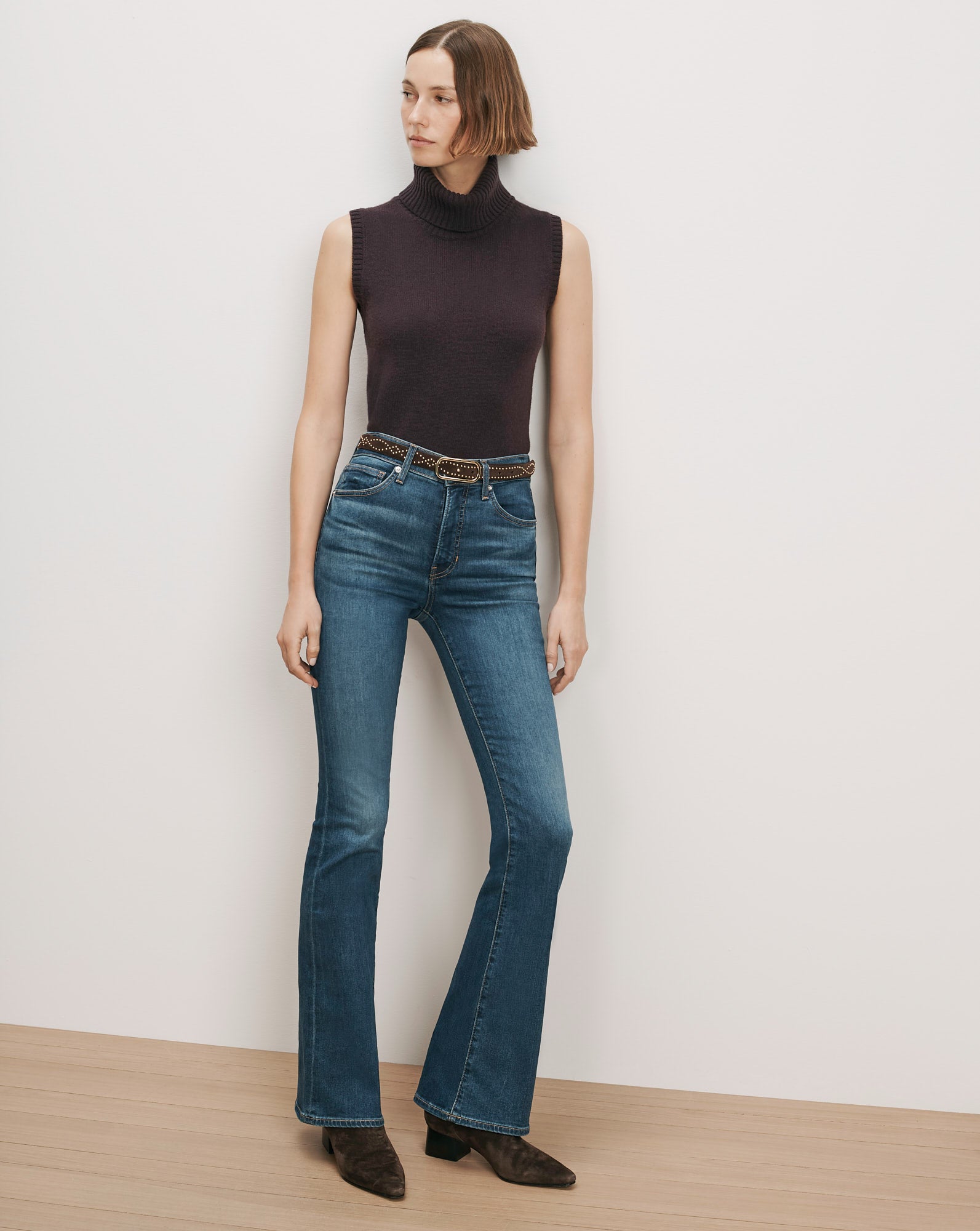 Veronica Beard Dark brown sleeveless turtleneck, blue flare jeans, studded belt.