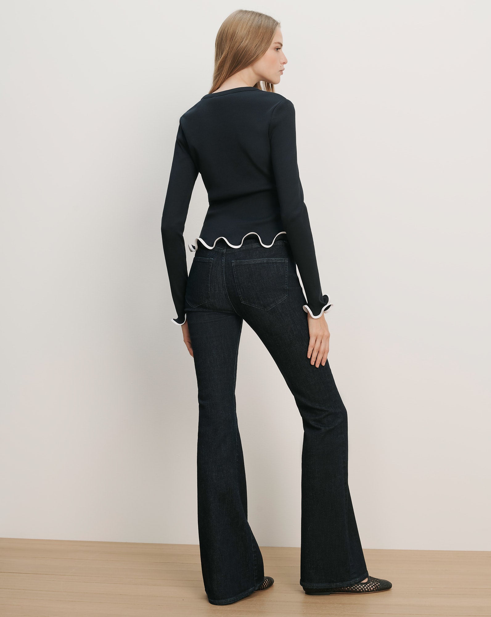 Veronica Beard Black long-sleeve top with white ruffled trim at the hem and cuffs, paired with dark wash flared jeans.